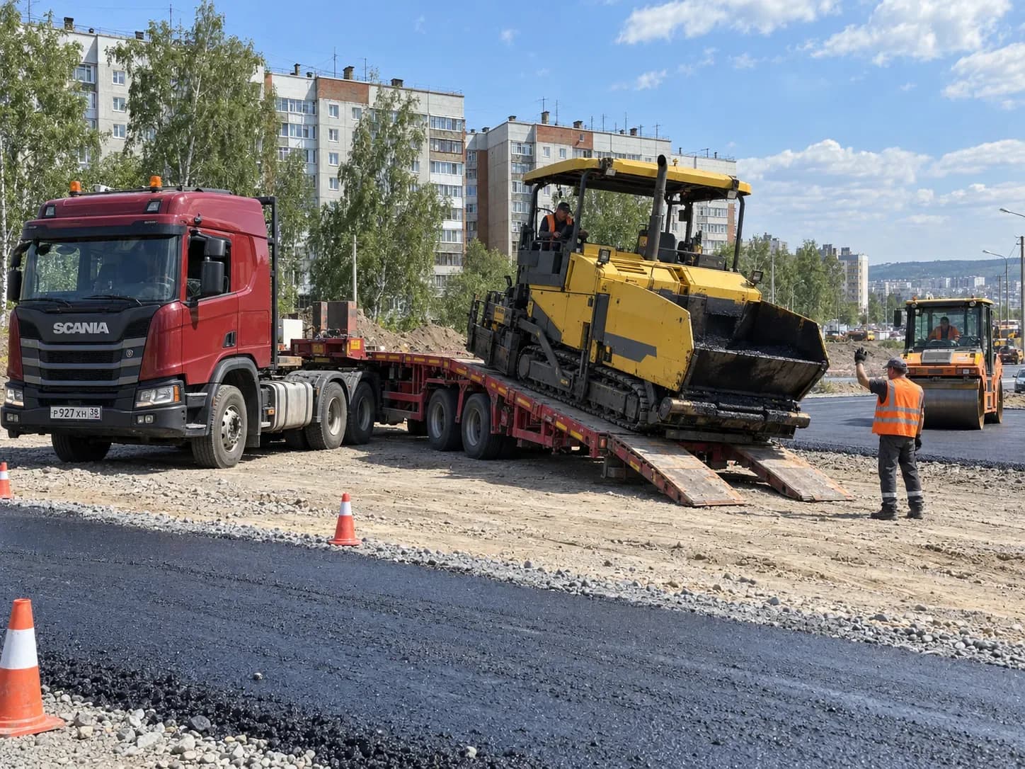 Асфальтоукладчик съезжает с трала на строительстве городской дороги