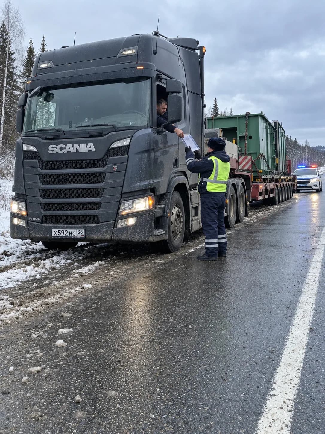Водитель тягача с негабаритным грузом передаёт инспектору ДПС документы на обочине трассы